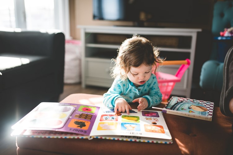 A young toddler reading a book at a table in the living room